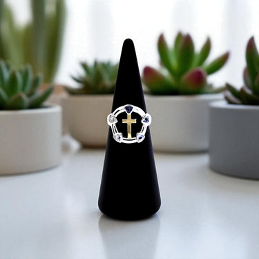 Ring with a cross design on a black stand in front of potted plants